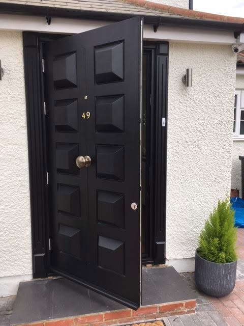 Black timber front door with raised panels and a brass centre knob, standing open