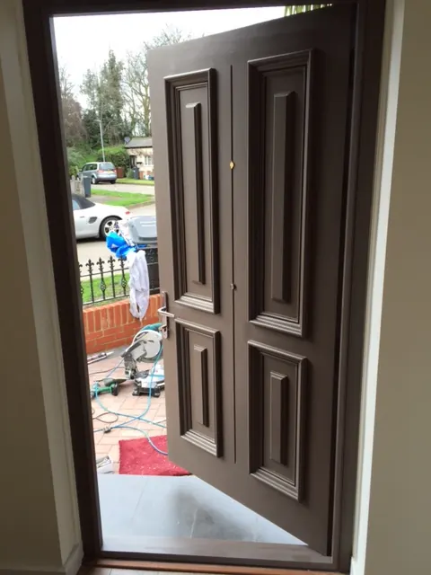 Interior view through an open mocha-brown panelled front door onto the street